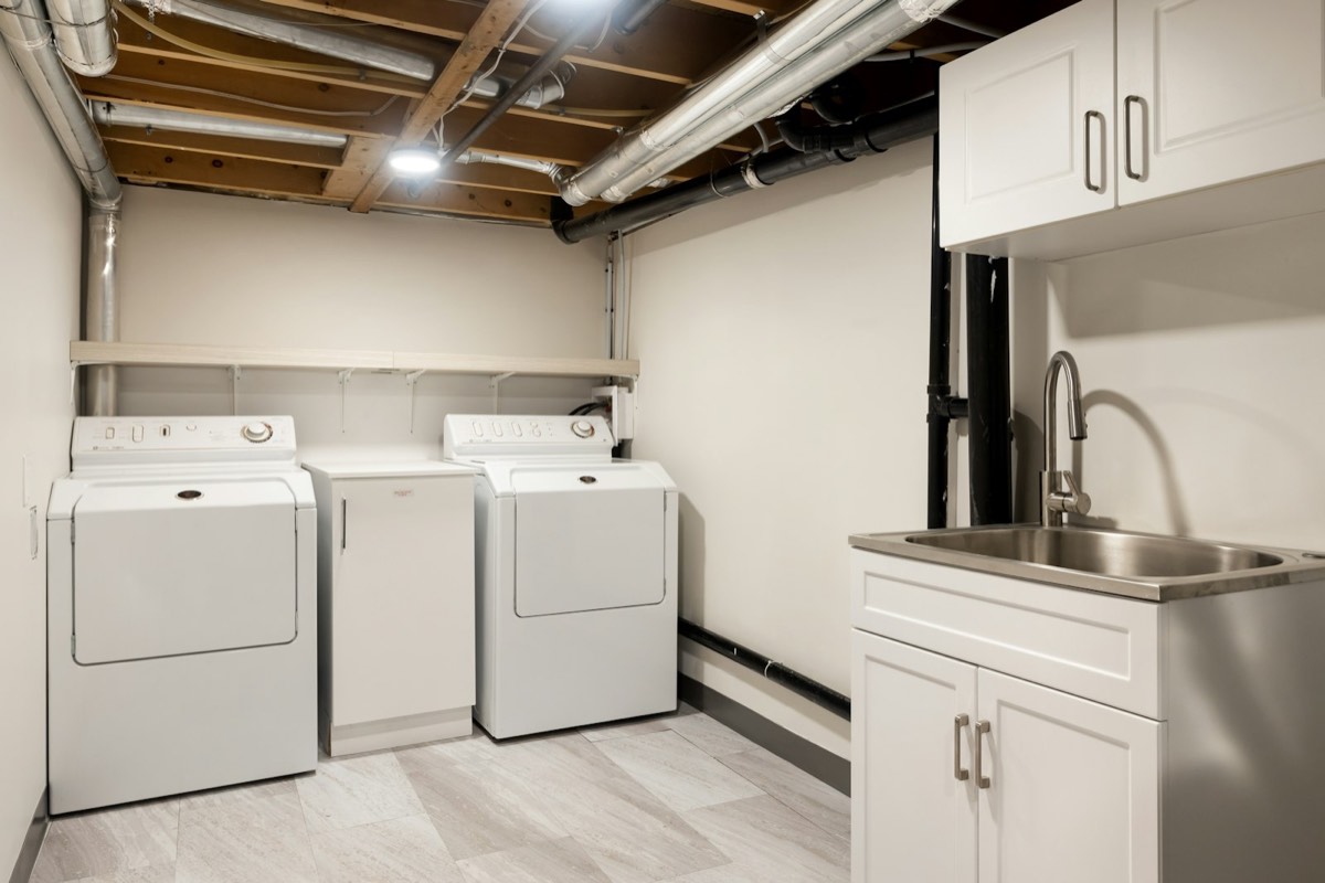 A basement laundry area with a washer, dryer and utility sink under exposed joists