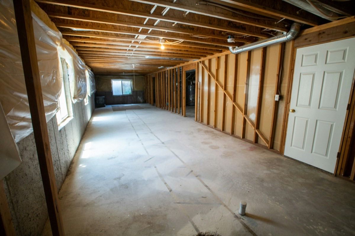 An unfinished basement with poured concrete foundation walls and a framed stud partition wall